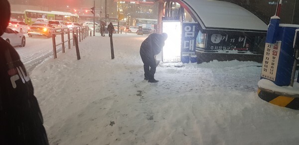 한 건물 앞 눈을 치우는 경비원이 보인다